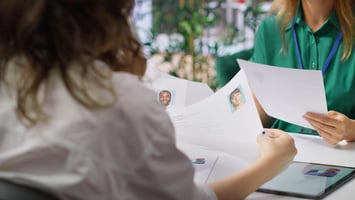 Hiring manager reviewing two candidate resumes with photos during recruitment process.