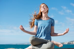 Beautiful woman meditating at the seaside sitting cross-legged on the rocks with her head tilted to the sun and her eyes closed in ecstasy-1