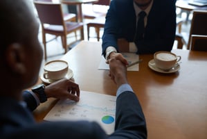 Two professionals shaking hands over documents and coffee, representing a successful salary negotiation meeting.