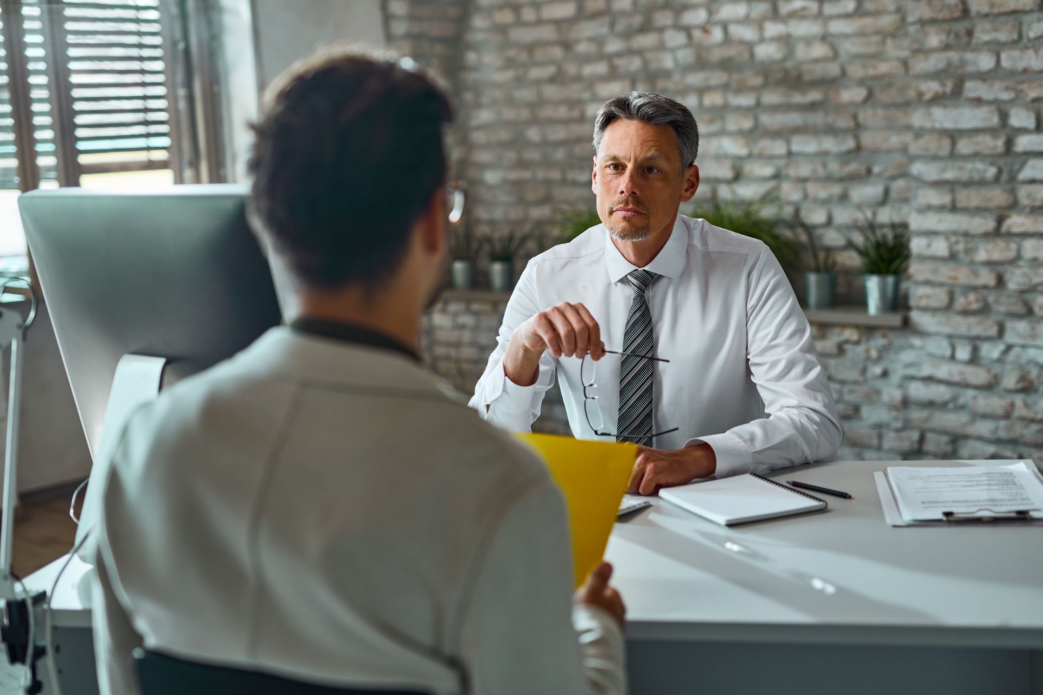 A professional manager in a tie looking serious while listening to an employee during a one-on-one salary meeting.