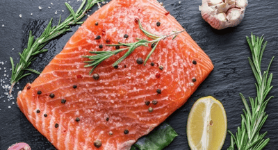 A fillet of salmon on a chopping board with other cooking ingredients